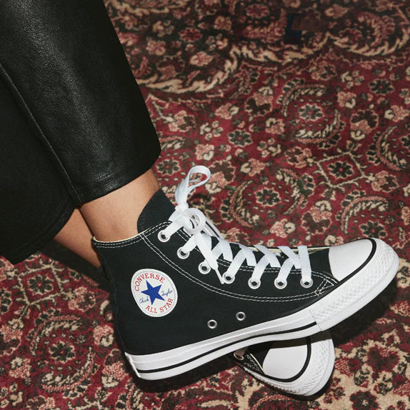 Black high-top sneakers with white laces on a patterned rug